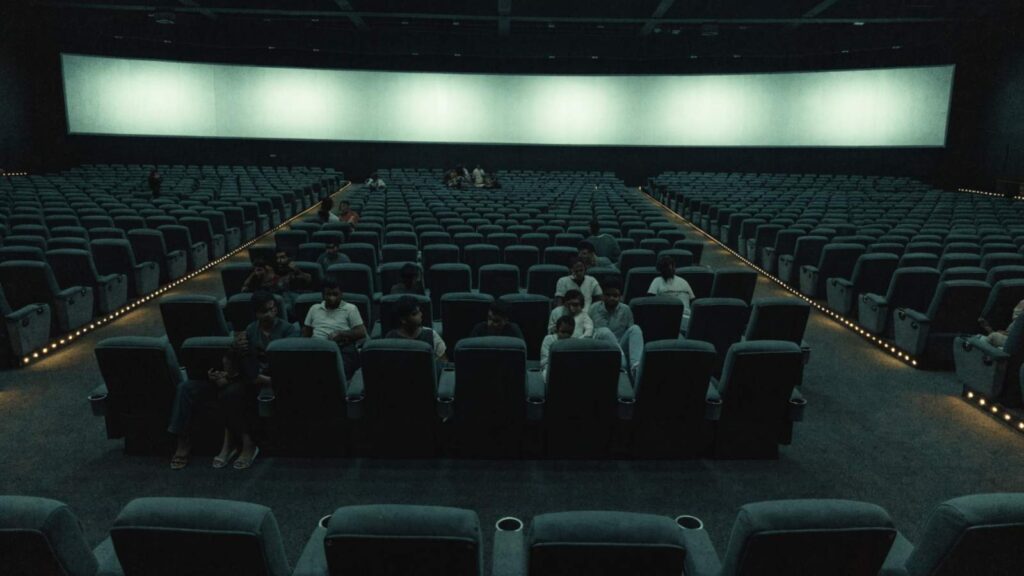 Rows of recliner seats in a large Indian multiplex with scattered clusters of people and many empty seats