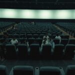Rows of recliner seats in a large Indian multiplex with scattered clusters of people and many empty seats