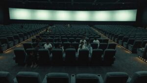 Rows of recliner seats in a large Indian multiplex with scattered clusters of people and many empty seats