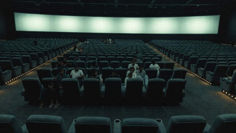 Rows of recliner seats in a large Indian multiplex with scattered clusters of people and many empty seats