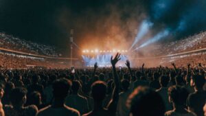 A vast night crowd with raised arms and phone lights facing a distant lit stage in an Indian stadium