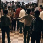 An animated crowd spilling out of a regional Indian cinema foyer into warm evening light