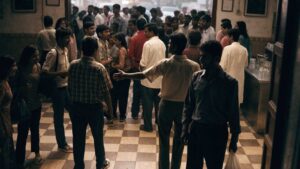An animated crowd spilling out of a regional Indian cinema foyer into warm evening light