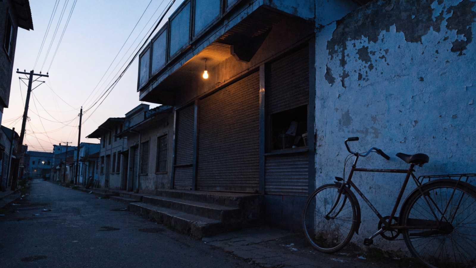 A shuttered small-town cinema with an empty ticket window and a single bulb over the door