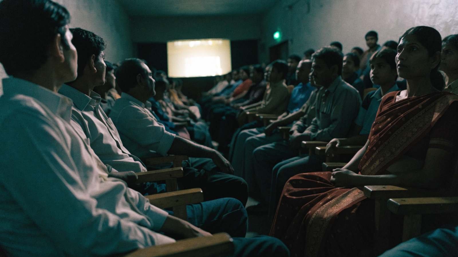 Local people of all ages in a Maharashtra town cinema, faces lit by the screen