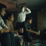 An Indian family crowded around a large television watching a floodlit cricket match at night