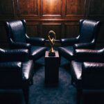 Four empty jury chairs facing away from a single gold trophy