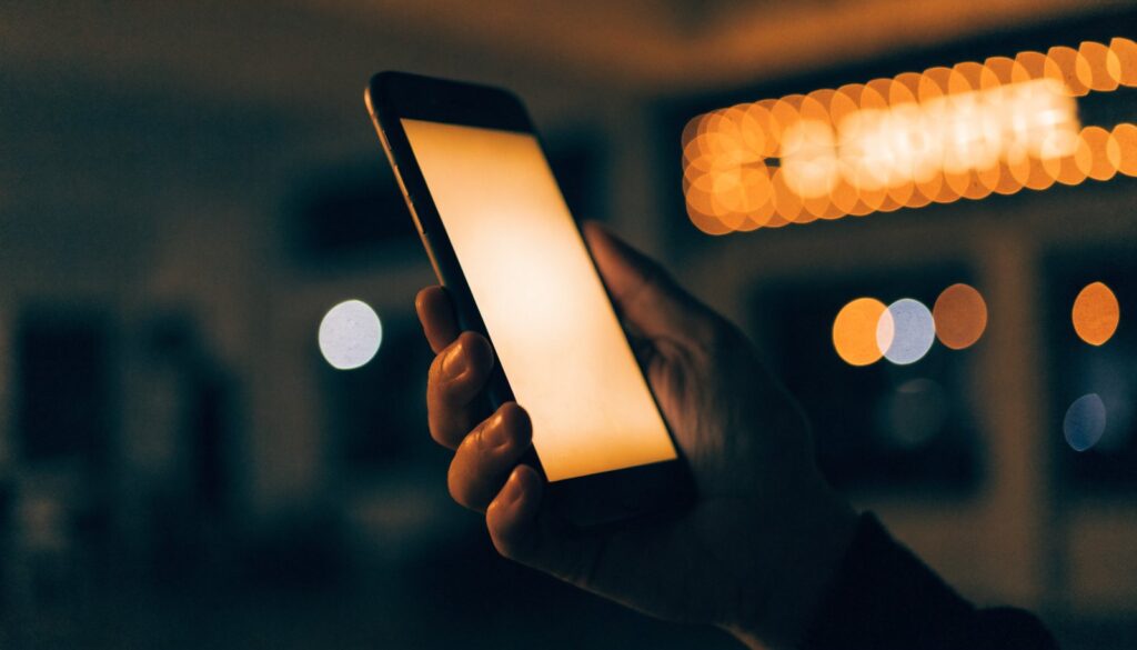 A glowing phone held in the dark against cinema lights