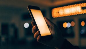 A glowing phone held in the dark against cinema lights