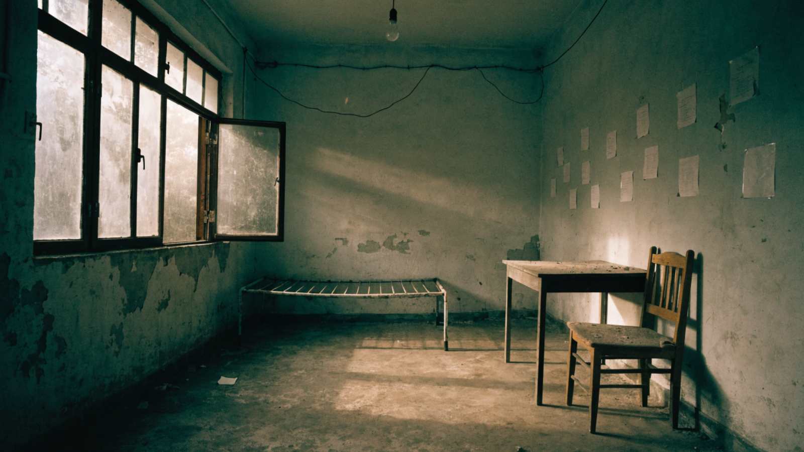 A bare cot, empty desk and dusty window in a vacated student hostel room