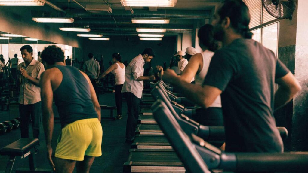 Men and women training on treadmills and free weights in a crowded Indian budget gym