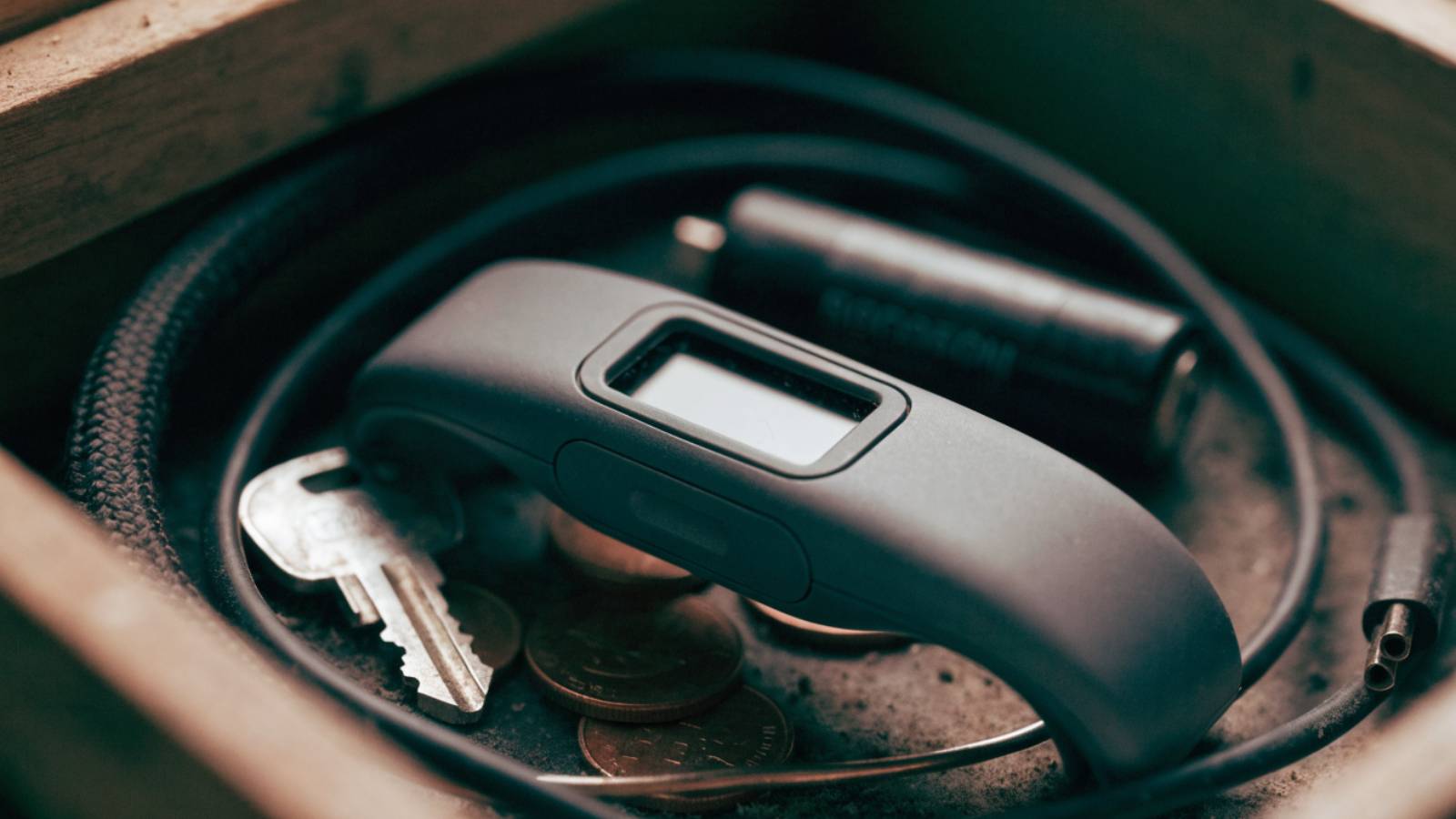 A cheap fitness tracker lying unused in a drawer among cables and coins