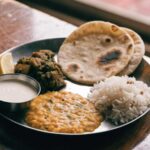 Dal, rice, roti, curd and a vegetable sabzi on a steel plate on a wooden table