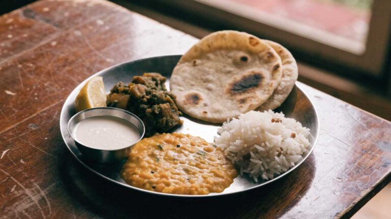 Dal, rice, roti, curd and a vegetable sabzi on a steel plate on a wooden table