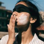 A young woman blending sunscreen into her cheek in bright direct sunlight