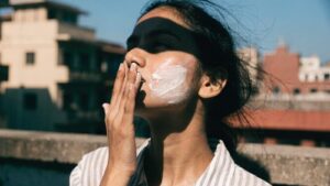 A young woman blending sunscreen into her cheek in bright direct sunlight