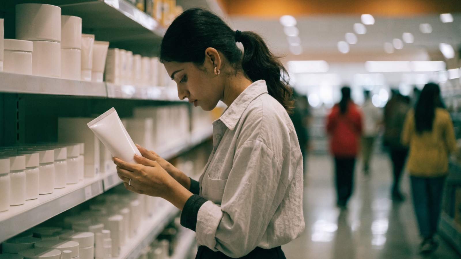 A shopper examining the back of an unbranded tube in a bright beauty aisle